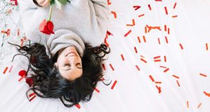 A woman lies on her bed, gently holding a rose, exuding serenity and elegance in a warm, cozy setting.
