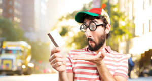 A man in a hat and glasses holds a credit card, appearing to make a transaction or financial decision.